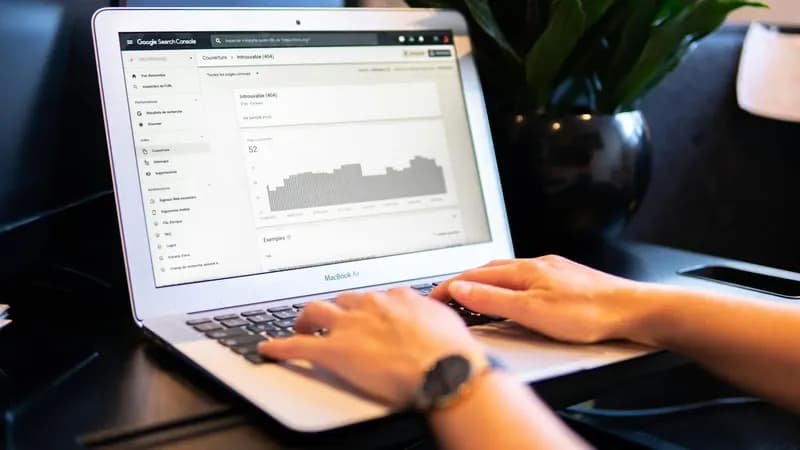 يدا شخص على لوحة مفاتيح حاسوب محمول تعرض شاشته لوحة Google Search Console مع تقرير وصور بيانية.